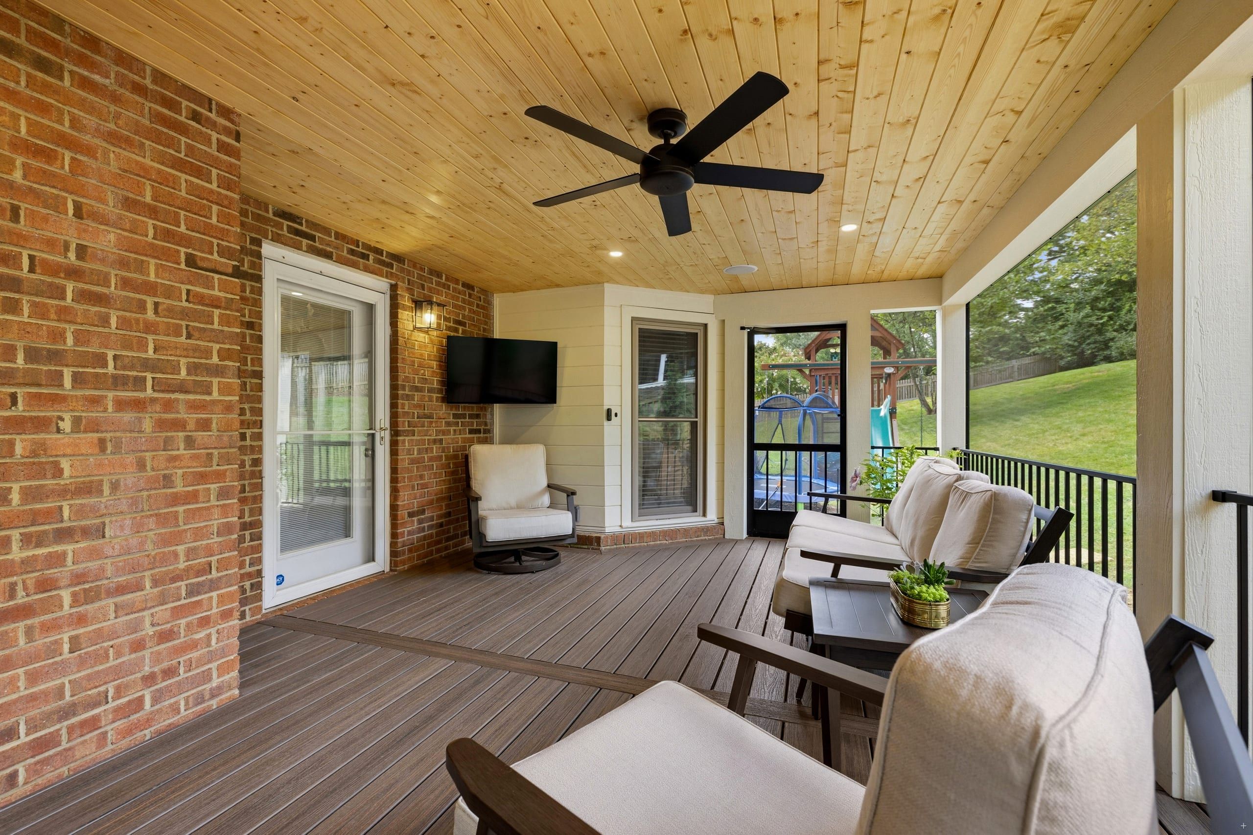 Ashgrove screened porch with a brick wall, white door into the home, mounted TV, and a screen door opening onto the side yard