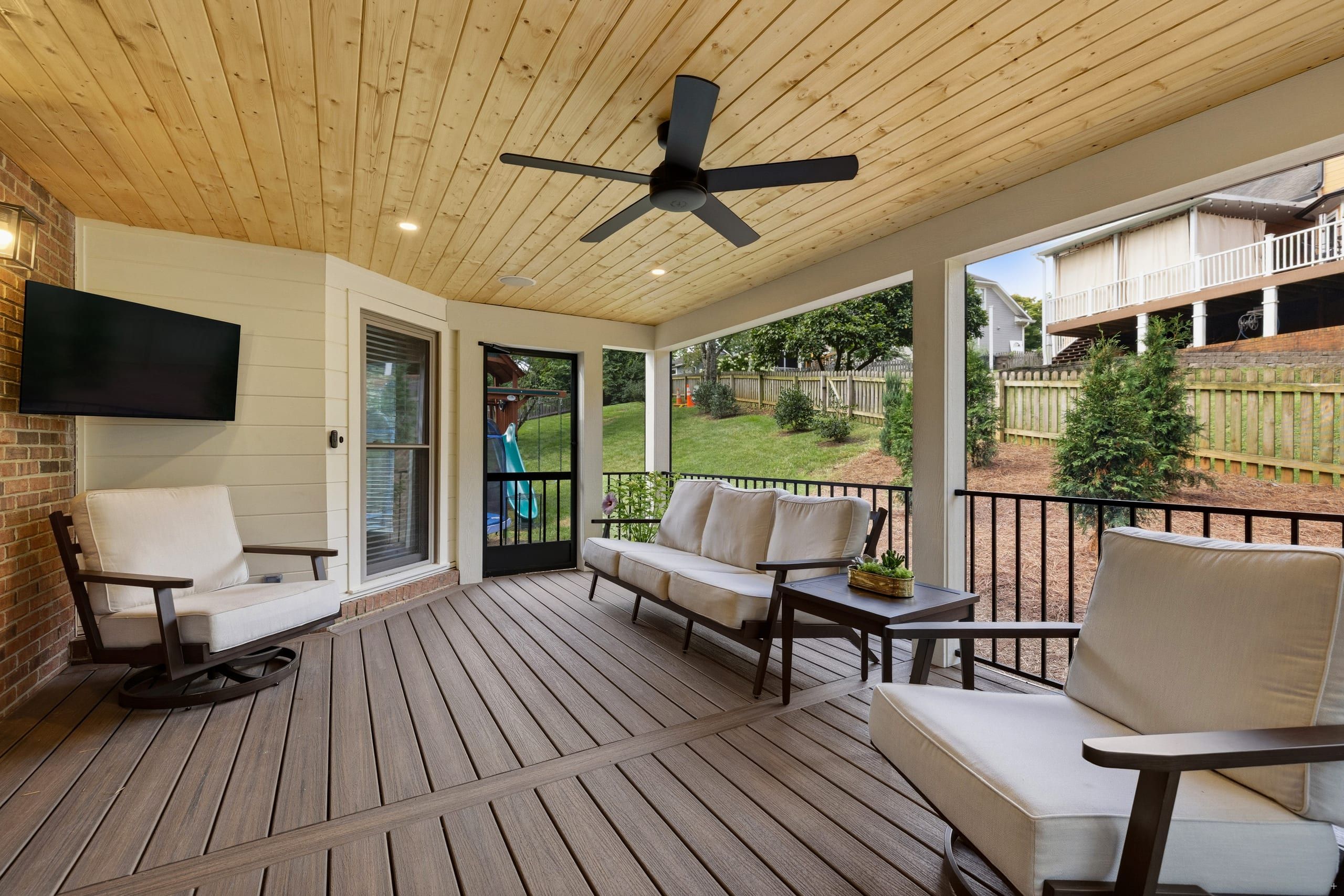 Seating area on the Ashgrove screened porch with a wood ceiling, ceiling fan, and black Fortress railing looking out to the backyard