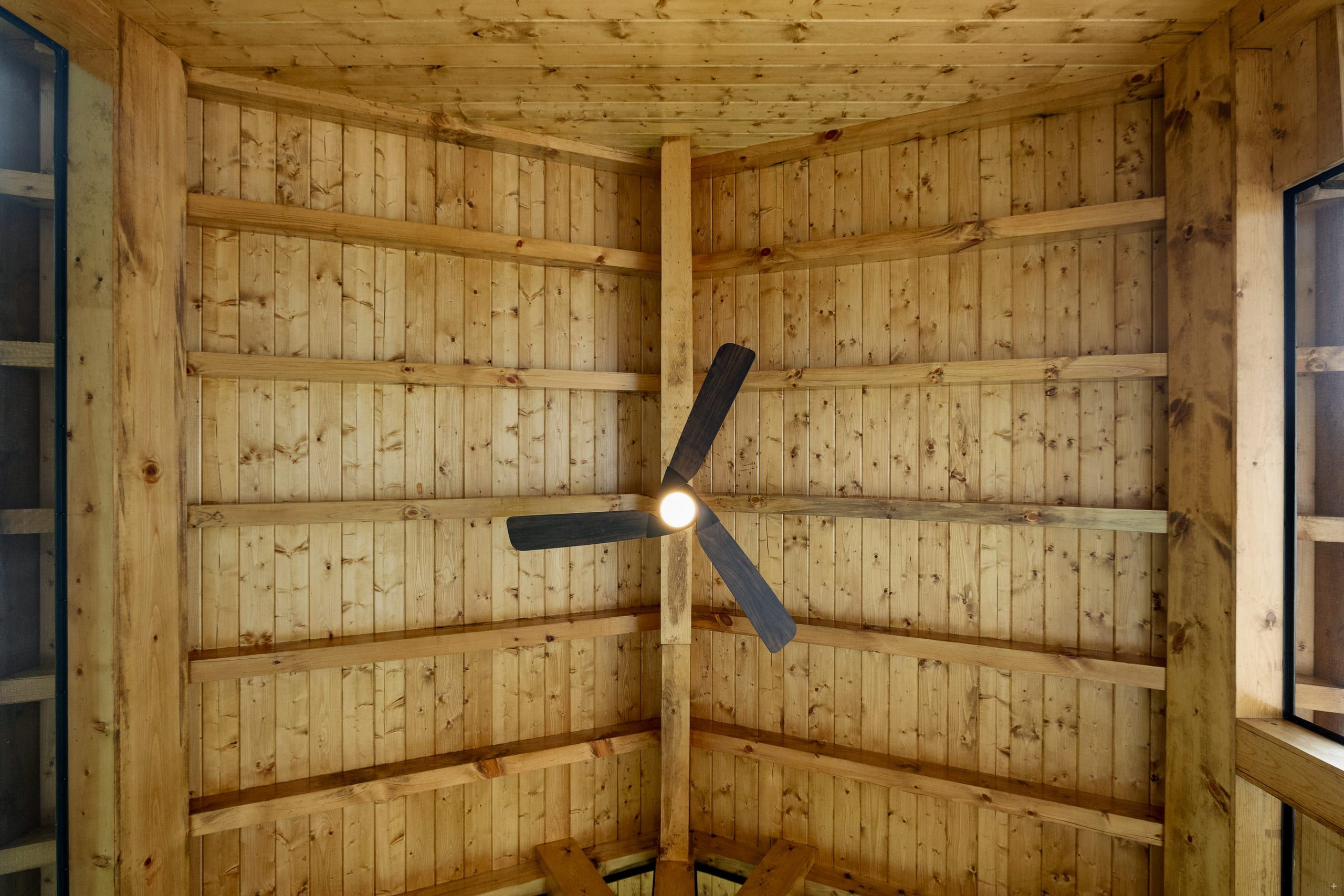 Looking up at the Venice porch's vaulted cedar tongue-and-groove ceiling with exposed beams and a dark ceiling fan